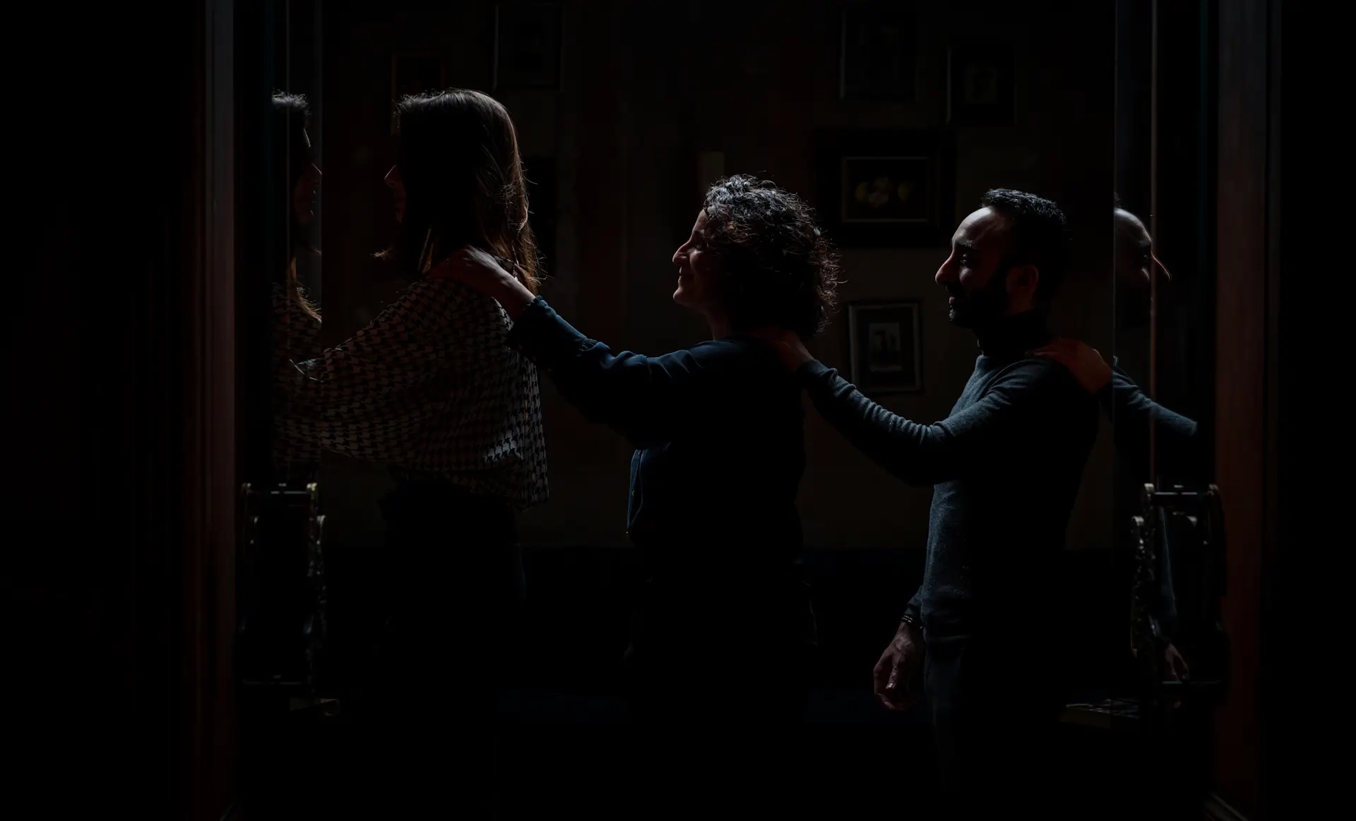 Three people walk in single file, each with a hand on the shoulder of the person in front, in a dark atmosphere evoking a sensory experience in the dark.