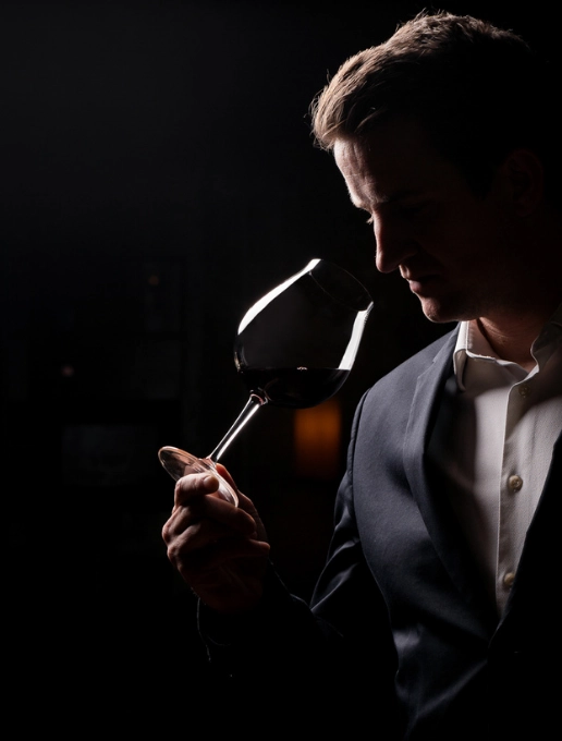 Hombre con traje oscuro oliendo vino tinto en una copa