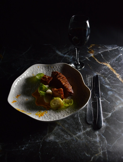 Plato y cubiertos con una copa de vino tinto sobre una mesa de mármol oscuro