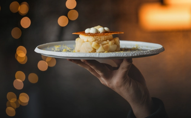 Dessert gastronomique dressé sur une assiette, servi à la main avec éclairage chaleureux et ambiance intimiste en arrière-plan.