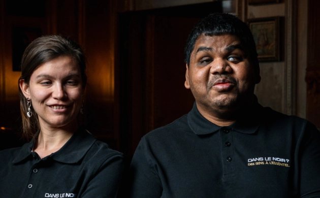 Deux membres de l'équipe Dans le Noir ?, souriants dans une salle à la lumière tamisée.