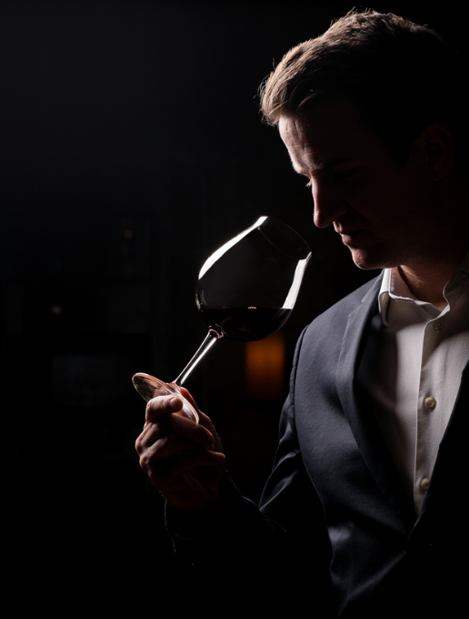 Hombre con traje oscuro oliendo vino tinto en una copa