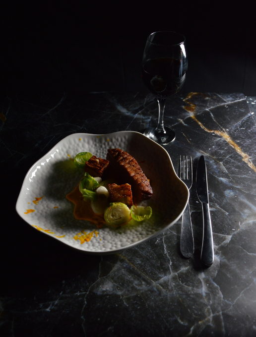 Plato y cubiertos con una copa de vino tinto sobre una mesa de mármol oscuro