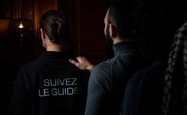 Expérience immersive dans le noir : un guide mène un groupe de participants, posant une main rassurante sur son épaule.