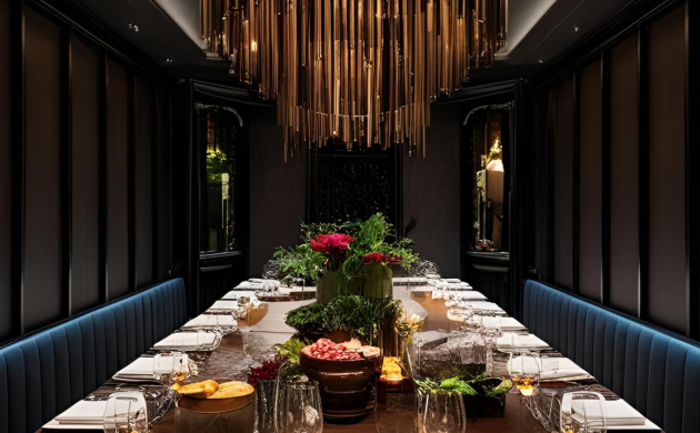 Salle immersive à l’ambiance feutrée, avec une longue table dressée de vaisselle raffinée et de fleurs sous un lustre doré majestueux.